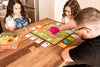 2 girls and a boy playing Gamewright Outfoxed on a wooden table